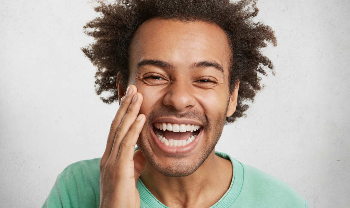 Positiveness and pleasant emotions concept. Glad man with dark healthy skin grins at camera, being happy to be praised by someone, feels proud of himself, poses in white studio. Overjoyed guy